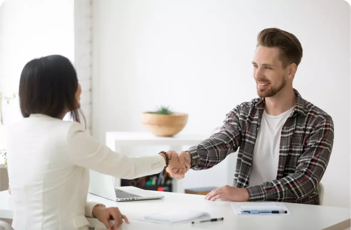 A man and woman shaking hands over a table.