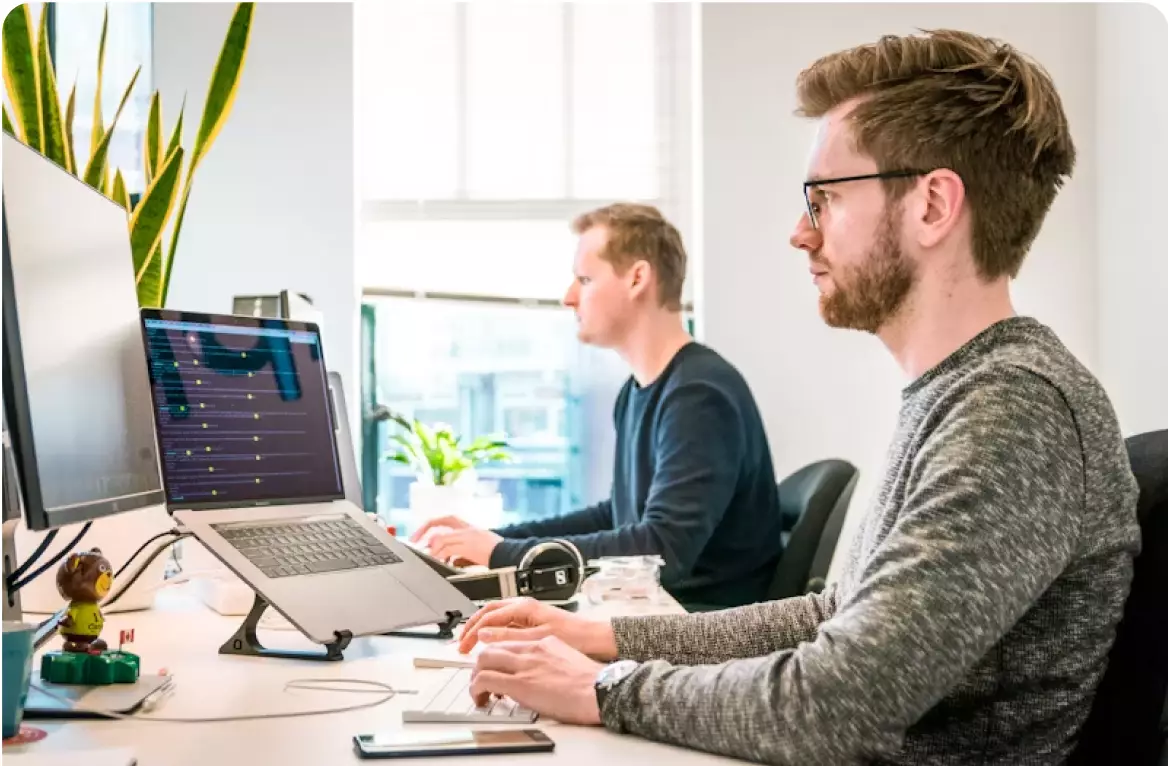 Two men sitting at a table with laptops.