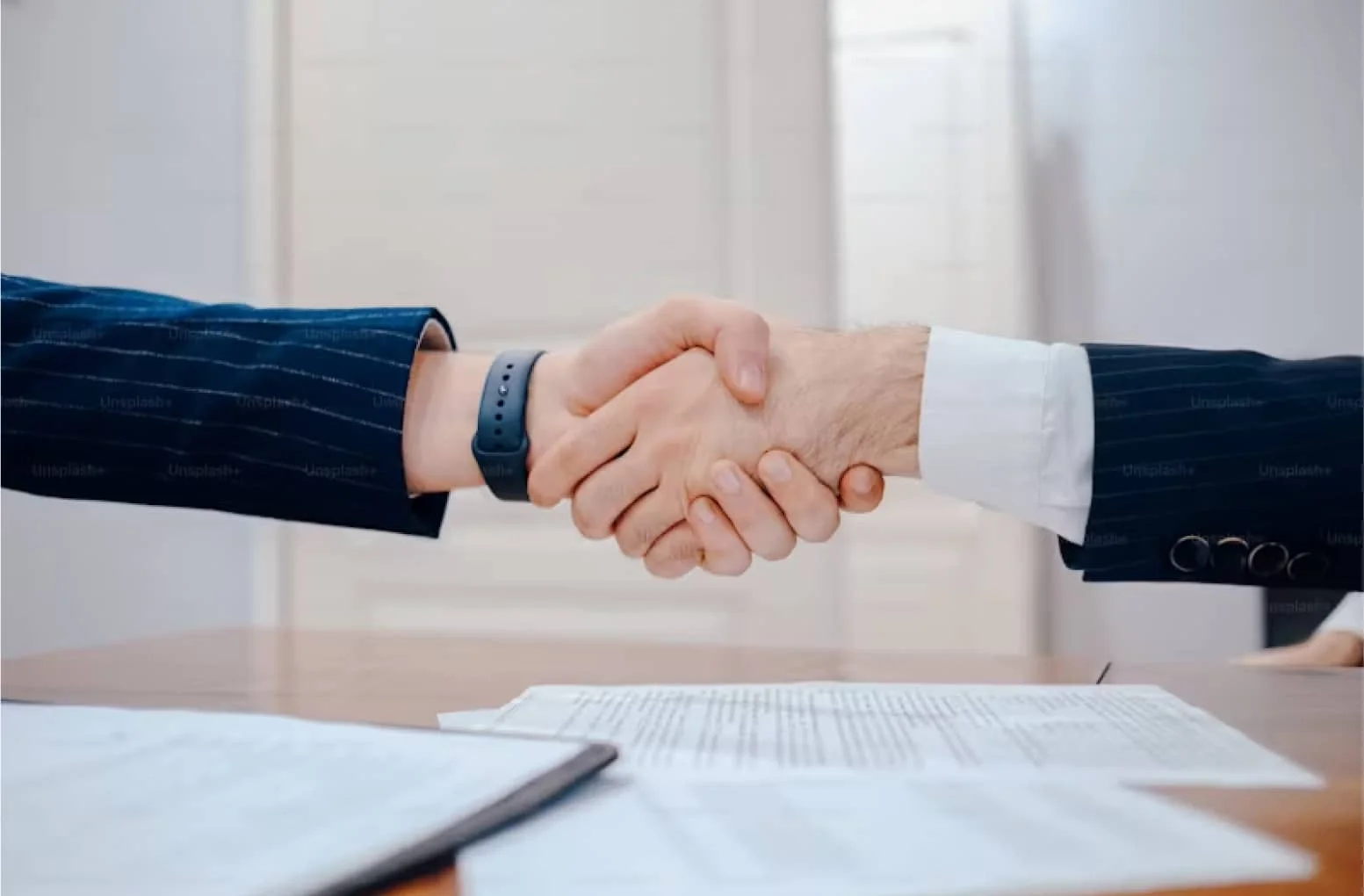 Two people shaking hands over a table with papers.